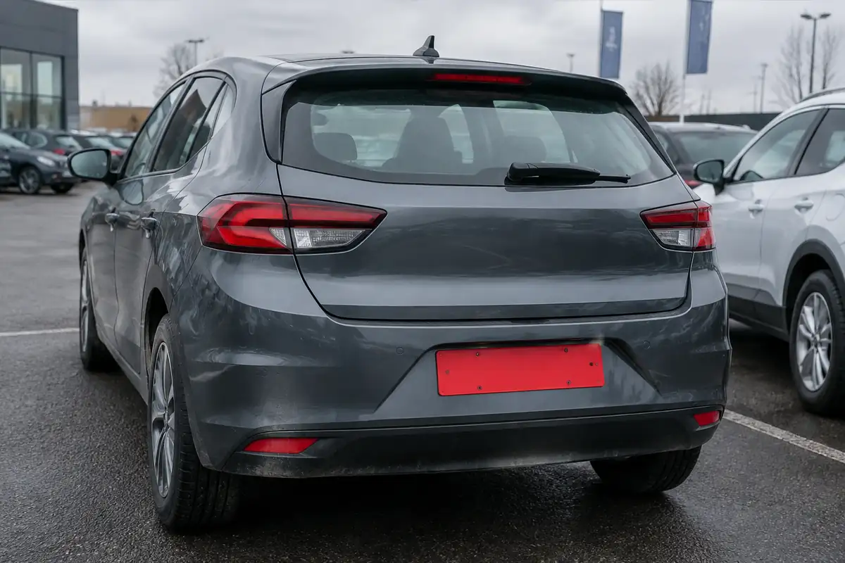 Arrière d'une voiture neuve avec une plaque rouge sur un parking de concession